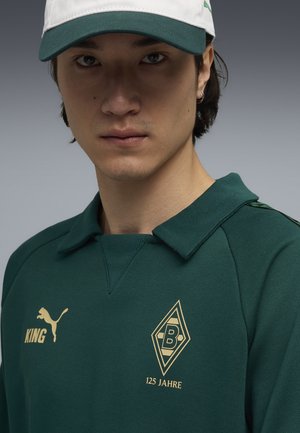 Grøn sweatshirts med krave, guld logo og teksten "125 ÅR." Inkluderer en hvid kasket med grøn skygge og Puma-logo.