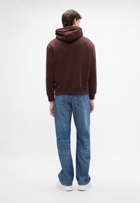 Brun hettegenser med snorhette, kombinert med lyseblå rette jeans. Antrekket har en avslappet passform og minimal detaljering.