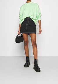 Sudadera verde de gran tamaño, falda corta de mezclilla negra con costuras blancas, botas gruesas negras con cordones y bolso negro pequeño.