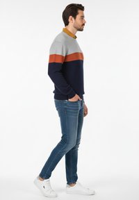 Jersey en rayas gris, óxido y marino; tejido suave con puños y cintura de canalé. Combinado con jeans ajustados azules y zapatillas blancas.