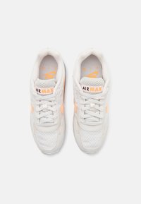 Baskets en maille blanche avec des accents orange, présentant un design à lacets et un logo Air Max visible sur la languette et sur le côté.