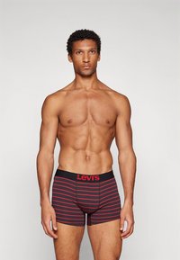 Moške boksarice Levi's v črni barvi z rdečimi vodoravnimi črtami. Opremljene z elastičnim pasom z logotipom "Levi's". Raztegljiv material, oprijet kroj.