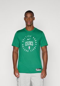 Camiseta verde de manga corta hecha de algodón. Presenta el logo de los Boston Celtics de la NBA y texto en blanco. Incluye la marca Nike. Corte estándar.