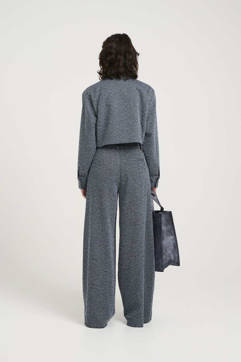Pantaloni ampi a zigzag grigi abbinati a una camicia cropped coordinata, accessoriati con una borsa tote in pelle nera.