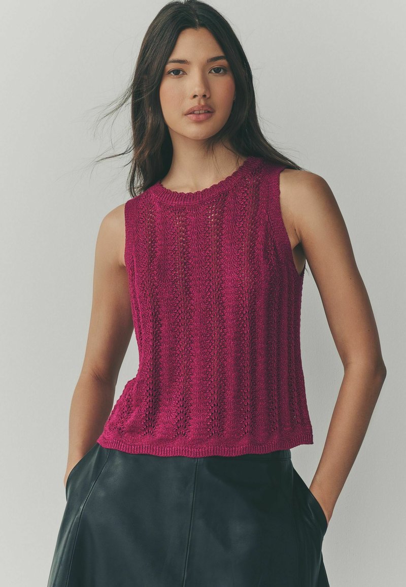 Fuchsia gestricktes ärmelloses Top mit einem strukturierten Muster, runder Ausschnitt und geripptem Saum. Kombiniert mit einem dunklen Lederrock.
