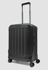 Valigia rigida nera con texture a costine verticali, manico retraibile, doppie ruote e chiusura laterale con cerniera.