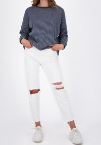 Camicia a maniche lunghe a righe navy abbinata a jeans bianchi strappati con strappi sulle ginocchia e orli grezzi, completata con sneakers bianche.