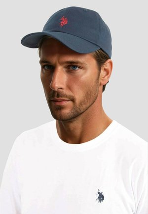 Navy baseball cap made of cotton, featuring red embroidered logo. Worn with a plain white t-shirt displaying a small navy logo on the chest.