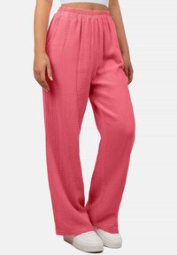 Rosa, strukturierte, weite Hosen mit elastischem Bund. Kombiniert mit weißen Sneakers. Der Stoff hat ein weiches, gekrepptes Design.