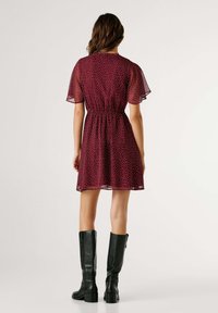 Vestido granate con lunares, mangas cortas transparentes, cintura elástica y falda acampanada, combinado con botas negras de cuero hasta la rodilla.