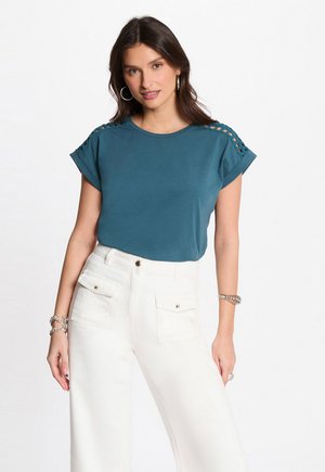 Teal short-sleeve t-shirt with shoulder cut-out details, paired with high-waisted white wide-leg pants featuring front pockets and square buttons.