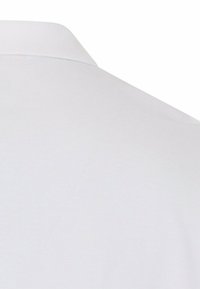 Close-up van de achterkant van de kraag en het schoudergedeelte van een effen wit overhemd met een gladde stof en eenvoudige stiksel.