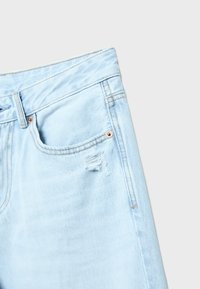 Lyseblå jeans i denim med forlommer, bæltestrop og en lille slidt rift nær lommen på en ensfarvet hvid baggrund.