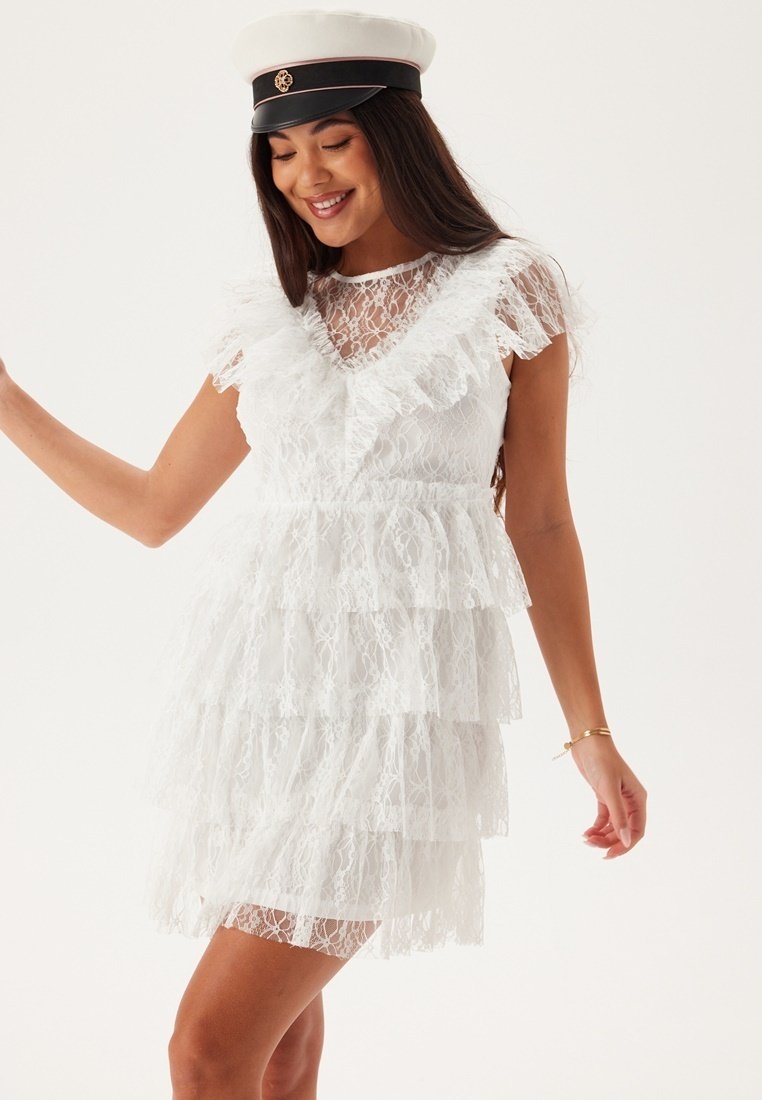 Abito bianco in pizzo con un design a strati e dettagli arricciati. Maniche corte e scollatura a girocollo, abbinato a un cappello coordinato.