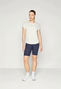 Lys grå, kortermet topp kombinert med marineblå sykkelshorts. Hvite joggesko og sokker fullfører den sporty stilen. Enkelt, tettsittende design.