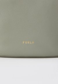 Világos zöld bőr táska texturált felülettel; arany "FURLA" logó részlettel rendelkezik. Minimalista dizájn, letisztult vonalakkal és látható hardver nélkül.