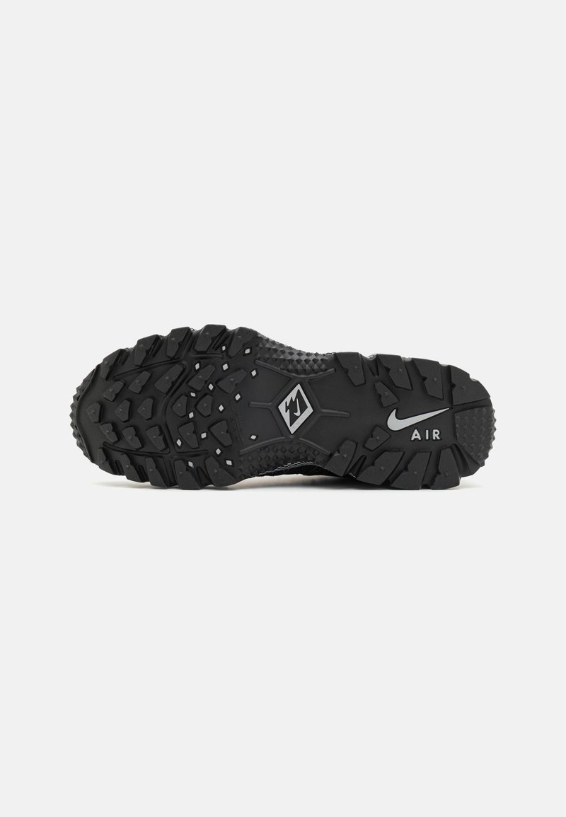 Semelle de chaussure de sport noire avec un design texturé, des rainures profondes pour une meilleure adhérence, et un logo Nike Air visible au niveau du talon.