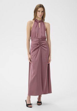 Femme portant une robe en satin mauve à col licou avec un détail froncé à la taille, debout devant un fond blanc uni.