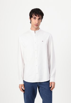 White long-sleeve shirt with a buttoned collar, featuring a small logo on the left chest. Light fabric with a smooth texture.