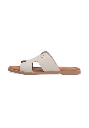 Beige slide sandal with cutout design, soft synthetic upper, and brown sole. Features a metallic accent near the arch for detail.