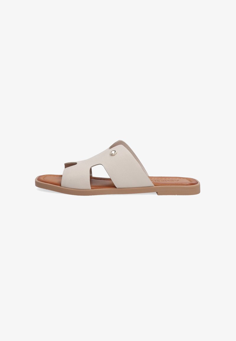 Beige slide sandal with cutout design, soft synthetic upper, and brown sole. Features a metallic accent near the arch for detail.