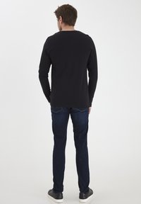 Sort langærmet skjorte med rund hals, parret med mørkeblå jeans og sorte sneakers. Glat stof, tætsiddende design, set fra bagsiden.
