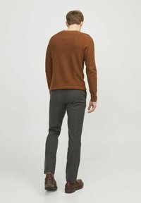 Brauner Strickpullover mit rundem Halsausschnitt, kombiniert mit schmal geschnittenen, dunkelgrauen Hosen. Braune Lederschuhe runden das Outfit ab.