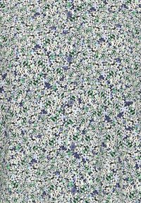 Nærbilde av stoff med små blomstermønstre i grønn, blå, hvit og svart, med en rad mørkeblå knapper nedover midten.