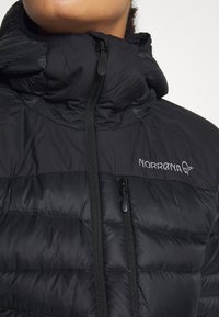 Black insulated puffer jacket with a high neck, featuring a central zipper and a small logo on the chest. Smooth texture and quilted pattern.