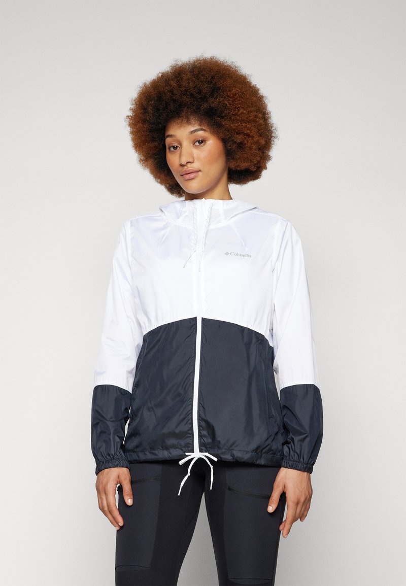 Die Windbreaker-Jacke hat einen weißen oberen Abschnitt und einen dunkelblauen unteren Abschnitt. Sie besteht aus leichtem Material mit elastischen Bündchen und einem gerafften Saum.
