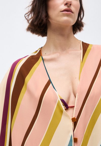 Γυναίκα που φοράει πολύχρωμη ριγέ μπλούζα με βαθύ ντεκολτέ σε σχήμα V και καφέ κουμπιά, εμφανίζοντας μερική στενή λήψη του λαιμού και του στήθους της.