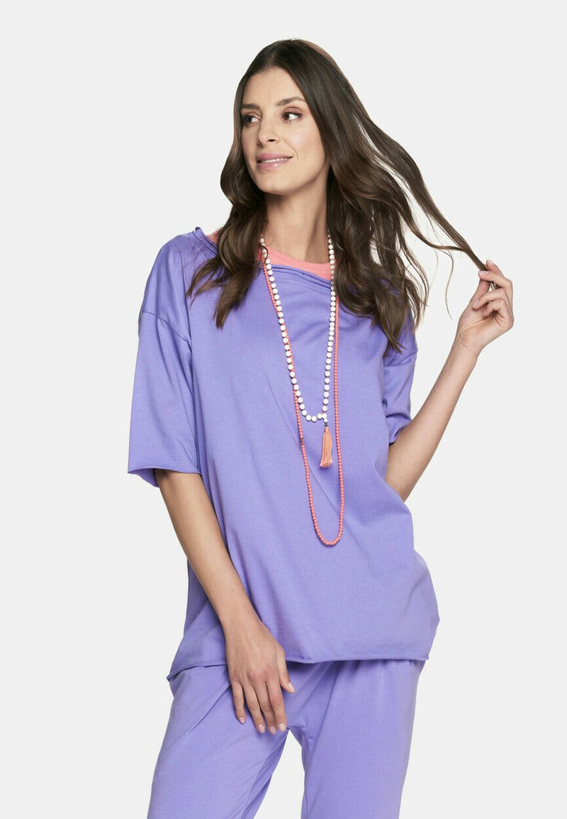 Luźna fioletowa bluzka z okrągłym dekoltem, z kontrastującą różową warstwą pod spodem. Połączona z dopasowanym fioletowym dołem.