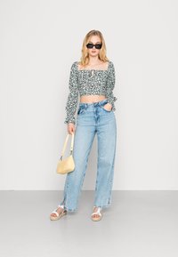 Top cropped floral com mangas bufantes, jeans de cintura alta azul claro, sandálias brancas e uma bolsa amarela clara.
