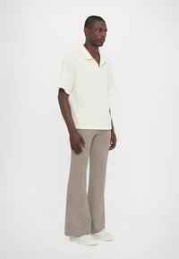 Kortärmad, krämfärgad polo med öppen krage, texturerad tyg, som är kombinerad med ljusbrun, utsvängd byxor och vita sneakers.