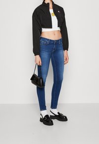 Chaqueta negra corta, top corto blanco con una carita sonriente, jeans ajustados azul, zapatos de plataforma negros, pequeño bolso negro con cadena.