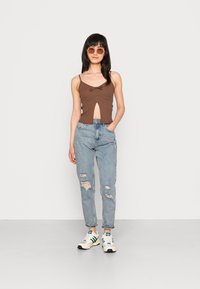 Top cropped castanho com um corte frontal, combinado com jeans claros desgastados e ténis brancos com detalhes verdes.