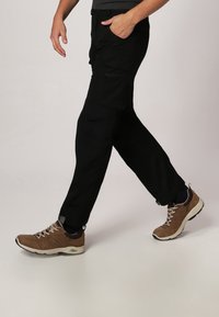 Pantalons cargo noirs avec de multiples poches, portés avec des chaussures de sport marron à lacets et une semelle grise, accompagnés d'un t-shirt gris.