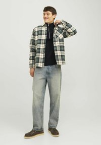 Karierte Bluse in Grün und Creme, geknöpft, mit einem beigen Kragen. Getragen über einem schwarzen Rollkragenpullover, kombiniert mit hellen Jeans und braunen Schuhen.