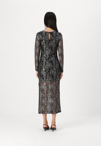 Robe en dentelle noire avec des motifs floraux argentés, manches longues, et un détail en ouverture dans le dos, présentant une silhouette ajustée jusqu'aux chevilles.