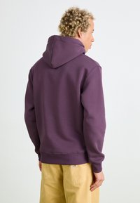 Sweatshirt à capuche violet avec une coupe décontractée, des poignets et un ourlet côtelés. Associé à un pantalon large beige clair avec des poches arrière.