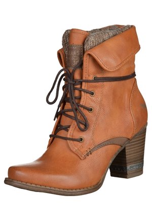 Botte cheville en cuir fauve avec talon empilé, lacets marron, revers plié et doublure en laine visible en haut.