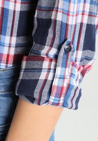 Lättviktig, rutig skjorta med mönster i blått, rött och vitt. Har en knäppt manschett och uppvikt ärm. Tillverkad av bomull med en avslappnad design.