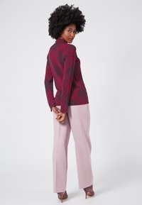 Maglione bordeaux a coste con un motivo a diamante, abbinato a pantaloni a palazzo rosa chiaro e scarpe con tacco taupe. Texture morbide in tutto.