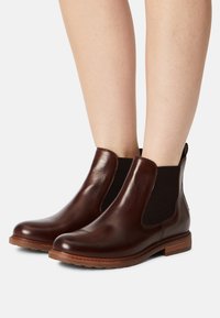 Bruna läder Chelsea-boots med elastiska sidopaneler, rund tå och låg staplad klack. Slät yta med texturerade accenter.