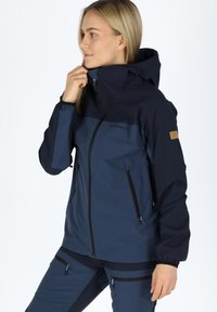 Navy blue waterproof jacket with a hood, featuring contrasting lighter blue panels, two zipped front pockets, and elastic cuffs.