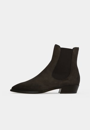 Botte Chelsea noire en daim avec panneau latéral élastique et petit talon empilé, vue de côté sur fond neutre.