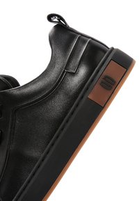 Czarny niski sneaker z cholewką ze skóry, czarną podeszwą, brązowym akcentem na pięcie oraz pętelką z tyłu.