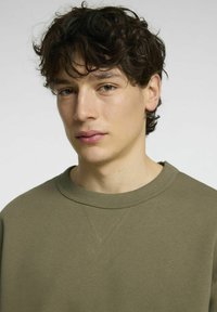 Olivgrön sweatshirt med rund halsringning, som har strukturerad sömnad vid axlarna och ett mjukt bomullstyg.