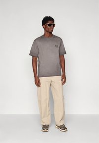 Grey cotton t-shirt with short sleeves, a small graphic on the chest, paired with beige loose-fitting pants and patterned sneakers.