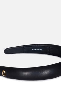 Un bandeau en cuir noir avec un logo doré devant et une surface intérieure texturée pour le confort. Étiquette de la marque visible sur la partie inférieure.